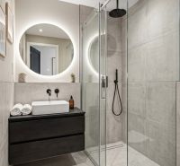 A bathroom in a studio apartment with a modern shower and a round mirror.