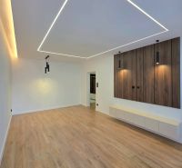 Living room with pendant lights and wood-patterned flooring in a three-room apartment.