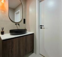 A bathroom with an oval mirror and a black sink in a 3-room apartment.