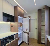 A kitchen with an opening dishwasher and refrigerator, wooden decor flooring in a 3-room apartment.