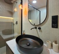 Bathroom in a 3-room apartment with an oval mirror, black sink, and shower.