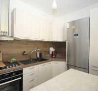 A kitchen in a 2-room apartment with a corner kitchen unit and a silver refrigerator.