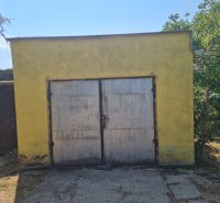 A yellow garage with metal doors near a family house in Komjatice, surrounded by trees.
