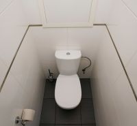 A toilet with white tiles and dark flooring in a 3-room apartment.