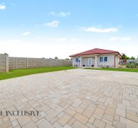 A family house in Vozokany with paving and a grassy garden, bordered by a concrete fence.