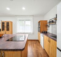 A kitchen with an island and a wooden decor floor in a family house.