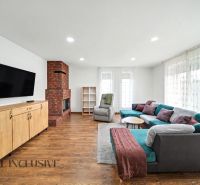 Living room in a family house with a fireplace, a wide sofa, and a wooden-patterned floor.
