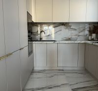 A kitchen in a 2-room apartment with white cabinets and marble tiles.
