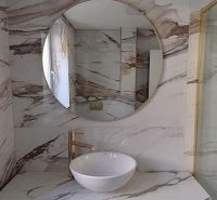 A bathroom with a marble wall and a round mirror in a 2-room apartment.