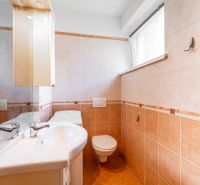 Bathroom in a studio apartment with a sink, cabinet, and toilet, light-colored tiled wall.