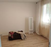 A room with a wooden floor decor, a pouf, and a lamp in a three-room apartment.