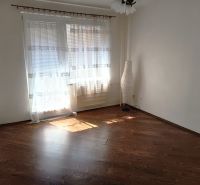 A room in a one-room apartment with a wooden decor floor and curtains.
