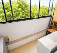 The interior of a balcony with a view of trees and seating area in a studio apartment.