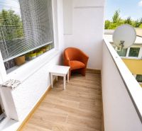 A balcony of a one-room apartment with an orange chair, a satellite dish, and flooring with a wood decor.