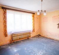 A room in a family house with worn walls, curtains, and a wall crucifix.