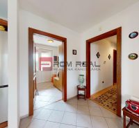 A hallway in a family house with decorations on the walls, white floor, and wooden doors.