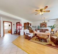 Living room in a family house with a wooden decor floor, a sofa set, and large windows.