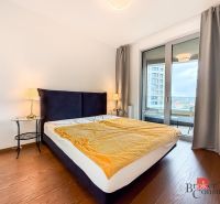 Bedroom in a 2-room apartment with a large bed, wood-patterned flooring, and a balcony.