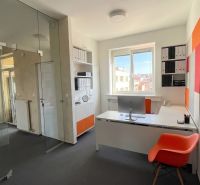 Offices with a glass partition, a desk, an orange chair, and a view from the window.