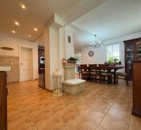 Dining room and kitchen with tiles, wooden furniture, and plant decorations in a family house.