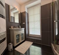 A bathroom in a family house with a sink, shower, and a window with a blind.