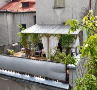 A furnished terrace with a canopy and plants, set in a green landscape.