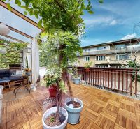The terrace of a 2-room apartment with a wooden decor floor, plants, and wooden furniture.