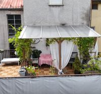 A terrace with a pergola and plants in a 2-room apartment, flooring with a wooden decor.