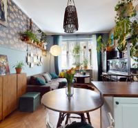 Living room with floral wallpaper, wooden decor flooring, and plenty of houseplants.