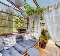 A furnished balcony with a sofa, cushions, and plants in a 2-room apartment.