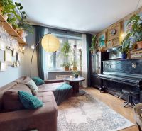Living room in a two-room apartment with a comfortable couch, a piano, and lots of plants.
