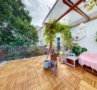 A balcony of a 2-room apartment with a wooden decor floor, plants, and a bench.