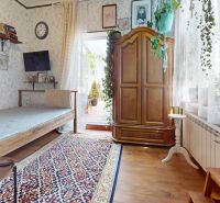 A room in a 2-room apartment with wooden decor, richly adorned with flowers and a traditional carpet.