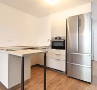 A kitchen in a studio apartment with a stainless steel refrigerator and wood-patterned flooring.