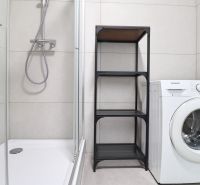 Shower corner, washing machine, and shelf in the bathroom of a studio apartment.