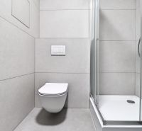Bathroom with toilet and shower in a studio apartment, with neutral tiles.
