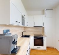 A kitchen with white cabinets, appliances, and a wood-patterned floor in a two-room apartment.