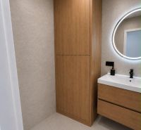 Bathroom with wooden furniture in a 2-room apartment, round mirror above the sink.