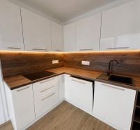 A kitchen in a 2-room apartment with white cabinets and a wooden decor floor.