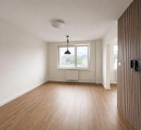 A room with a wooden decor floor and large windows in a 2-room apartment.