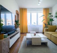 Living room in a 2-room apartment with a wooden decor floor and yellow curtains.