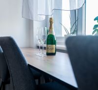A dining table with a bottle of sparkling wine, two glasses, and a plant in a two-room apartment.