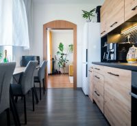 The kitchen of a 2-room apartment with black tiles and a wooden decor floor.