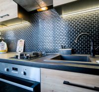 Modern kitchen with black tiles and wooden decor in a 2-room apartment.