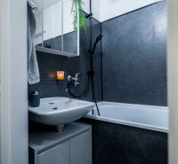 Bathroom in a 2-room apartment with a bathtub and gray tiles.