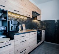 A kitchen in a 2-room apartment with a wooden decor floor and black tiles.