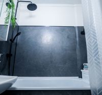A bathroom with dark walls, a showerhead, and a white bathtub in a 2-room apartment.