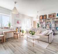 Living room in a two-room apartment with a wooden decor floor, a bookshelf, and a sofa.