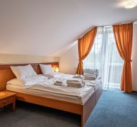 A bedroom with a double bed, orange curtains, and a table in a family house.