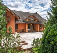 A family house in Veľká Lomnica with a garden and a wooden terrace surrounded by coniferous trees.